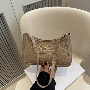 Beige woven texture handbag with golden bow accent shown in a hand-held indoor setting