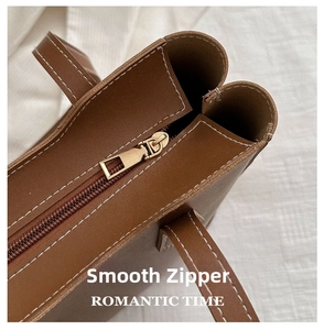 Détail d'un sac cabas en cuir marron avec fermeture éclair dorée et coutures blanches