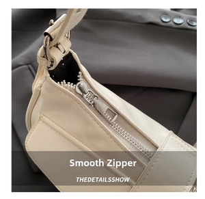 Detail of smooth metal zipper and cream faux leather texture on minimalist shoulder bag