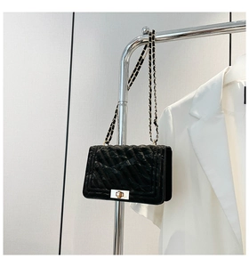 Detail of black quilted leather crossbody bag with gold chain strap and turn-lock closure