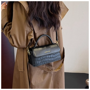 Detail of black crocodile texture leather bag with gold buckle and adjustable strap