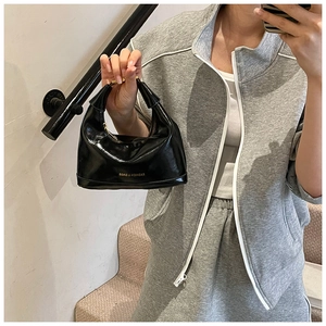 Detailed shot of glossy black patent leather bag featuring mirror fashion text and metal hardware