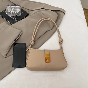 Minimalist beige baguette bag with knotted straps and gold clasp over aesthetic books