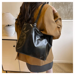 Dettaglio della borsa tote in pelle nera lucida con fibbia metallica e riflessi