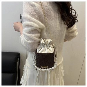 Detail of elegant drawstring bucket bag featuring a large pearl handle and metallic chain strap
