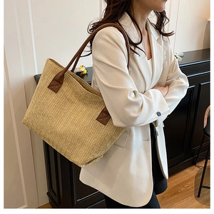 Dettaglio di una borsa tote in paglia intrecciata kaki con manici in pelle marrone scuro