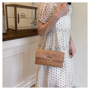Modella che indossa una borsa in paglia vintage con tracolla a catena e fibbia dorata