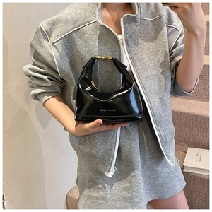 Detail of glossy black patent leather dumpling bag with gold zipper and fashion text