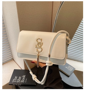 Close-up of white leather square bag featuring golden logo and metallic tassel details