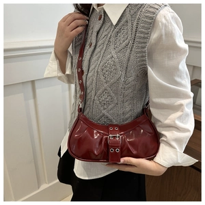 Detail of burgundy glossy patent leather underarm bag with silver eyelets and buckle