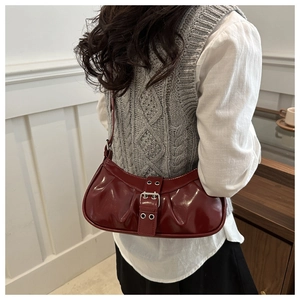 Detail of dark red patent leather crescent bag with vintage pleated texture and buckle strap