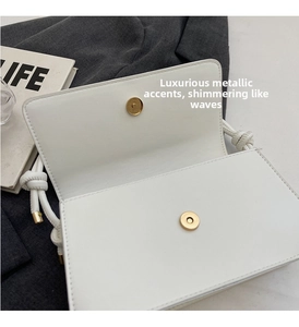 Detailed shot of white leather square bag featuring golden magnetic buckle and knotted strap
