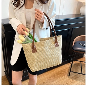 Dettaglio borsa tote in paglia intrecciata con manici in pelle marrone tenuta da modella
