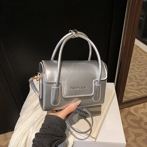 Petit sac carré argenté avec fini métallique et bandoulière amovible tenu à la main
