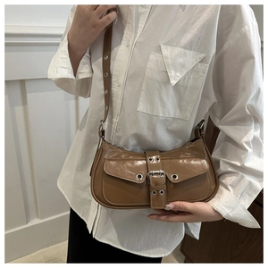 Detail of a brown patent leather shoulder bag featuring silver grommets and belt buckles
