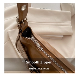 Detailed close-up of a brown patent leather shoulder bag with smooth silver metal zipper