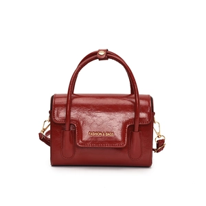 Deep red patent leather handbag with gold accents and top handle in a minimalist square design