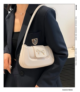 Creamy white shoulder bag with golden bow buckle detail shown on a model