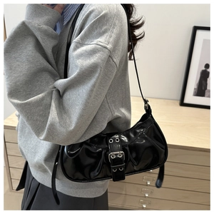 Close-up of black glossy shoulder bag with silver metal buckles and eyelets detail