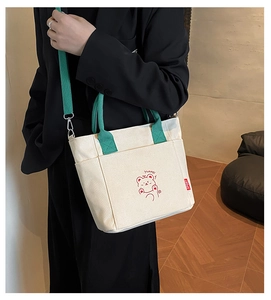 Detail of off-white canvas tote with green handles and a red cartoon bear design