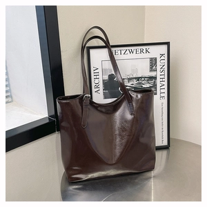 Detail of dark brown glossy vintage tote bag with adjustable strap on a metal surface