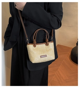 Dettaglio della borsa in paglia intrecciata con manici in pelle marrone indossata
