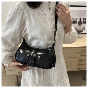 Close-up of black glossy Y2K shoulder bag with silver buckle worn with white lace dress