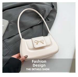 Detailed close-up of cream shoulder bag with a polished gold-tone bow metal clasp