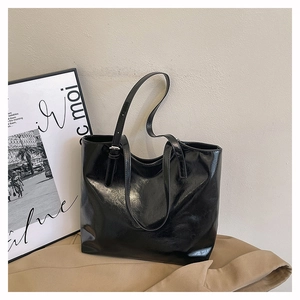Detail of glossy black leather tote bag with side metal buckle on a beige backdrop