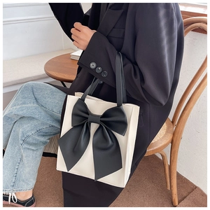 Detail of a beige tote bag with a large black bow accent and slim leather handles