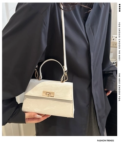 Detail view of cream white textured handbag with gold twist lock on black shirt