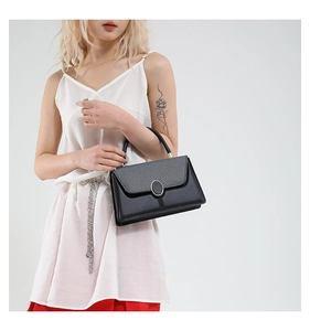 Close-up of black handbag with mixed leather textures and golden oval metal buckle