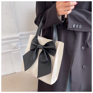 Detail showing high-quality leather texture and large decorative black bow on tote bag