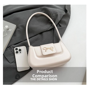 Chic cream crescent shoulder bag with golden bow buckle detail on a grey blazer