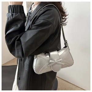 Détail du sac à bandoulière argenté avec nœud porté sur une veste en cuir noir