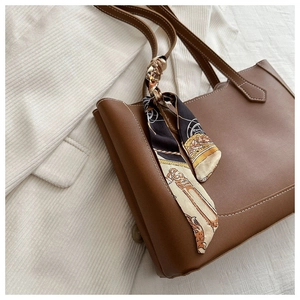 Détail d'un sac cabas en cuir marron avec un foulard décoratif et des surpiqûres