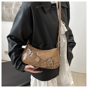 Brown crescent shoulder bag with metallic buckle straps shown on a model with leather jacket