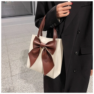 Detail of a beige tote bag with a large bow decoration and dark brown handles