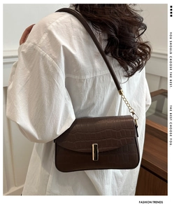Detail of dark brown croc-embossed shoulder bag with elegant gold metal latch closure