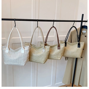 Detail view of woven tote bags in four colors: white, beige, brown, and black hanging on a rack