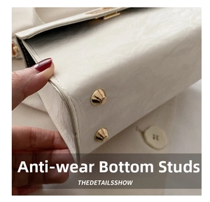 Detail view of white textured leather bag bottom featuring gold metal protective studs