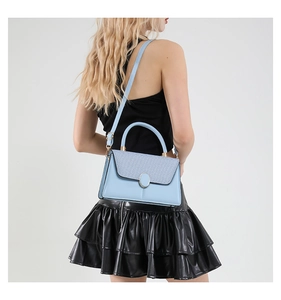 Detail of light blue embroidered tote bag with oval metal buckle and textured flap