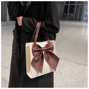 Detail of a beige tote bag with a large brown bow and contrasting straps on a black coat