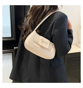 Close-up of a cream shoulder bag featuring a metallic gold bow buckle and smooth leather