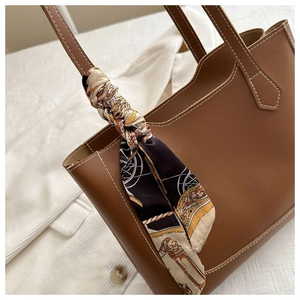 Détail de la poignée du cabas marron avec un foulard en soie à motif vintage enroulé