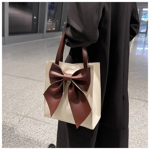 Detail of off-white tote bag featuring a large brown bow and premium leather texture