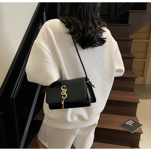 Detail of a black leather square crossbody bag featuring a gold S-shaped logo and tassels