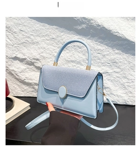 Detail view of the sky blue handbag showing woven texture flap and golden round buckle
