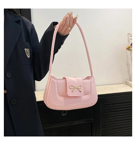 Detail of a pink underarm bag featuring a metallic gold bow on smooth faux leather