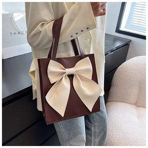 Detail view of large dark brown tote bag with a contrasting creamy white bow decoration